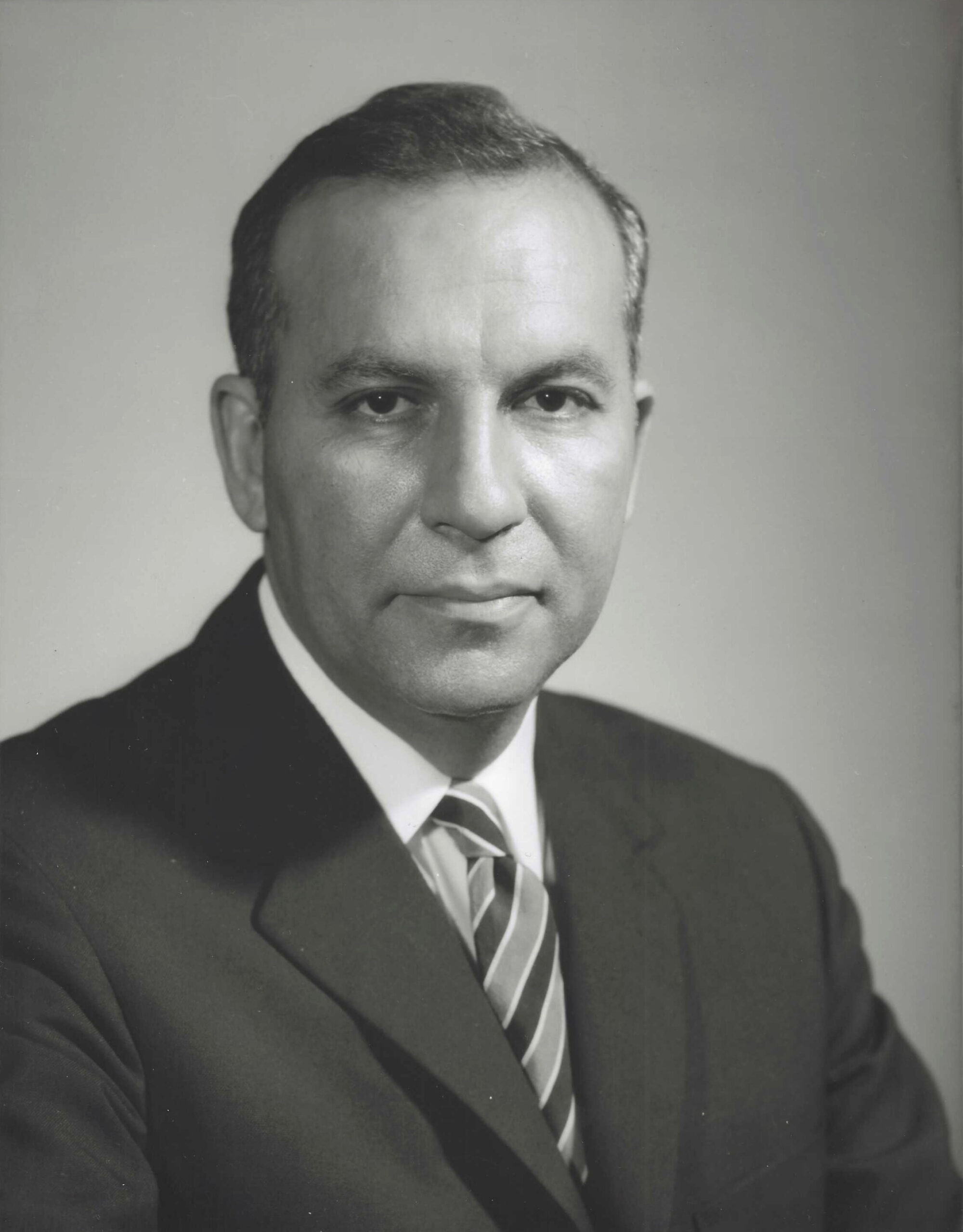 Black and white portrait of a man in a suit with a tie, looking confidently at the camera,